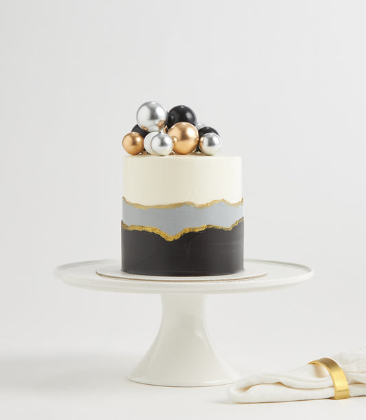 Luxe Black Forest birthday cake with charcoal and cream layers, gold accents, and metallic spheres on white stand