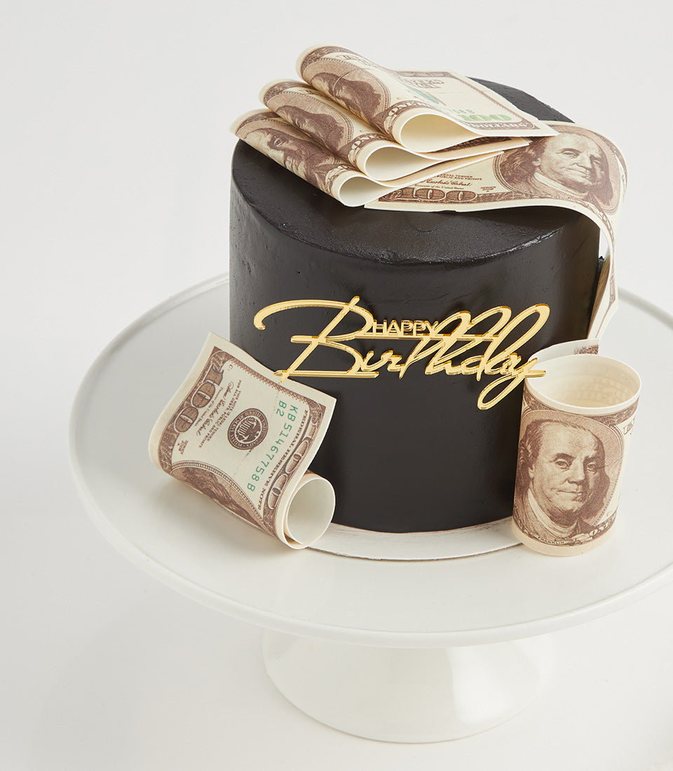 Black cylindrical layer cake with edible money design and gold Happy Birthday topper