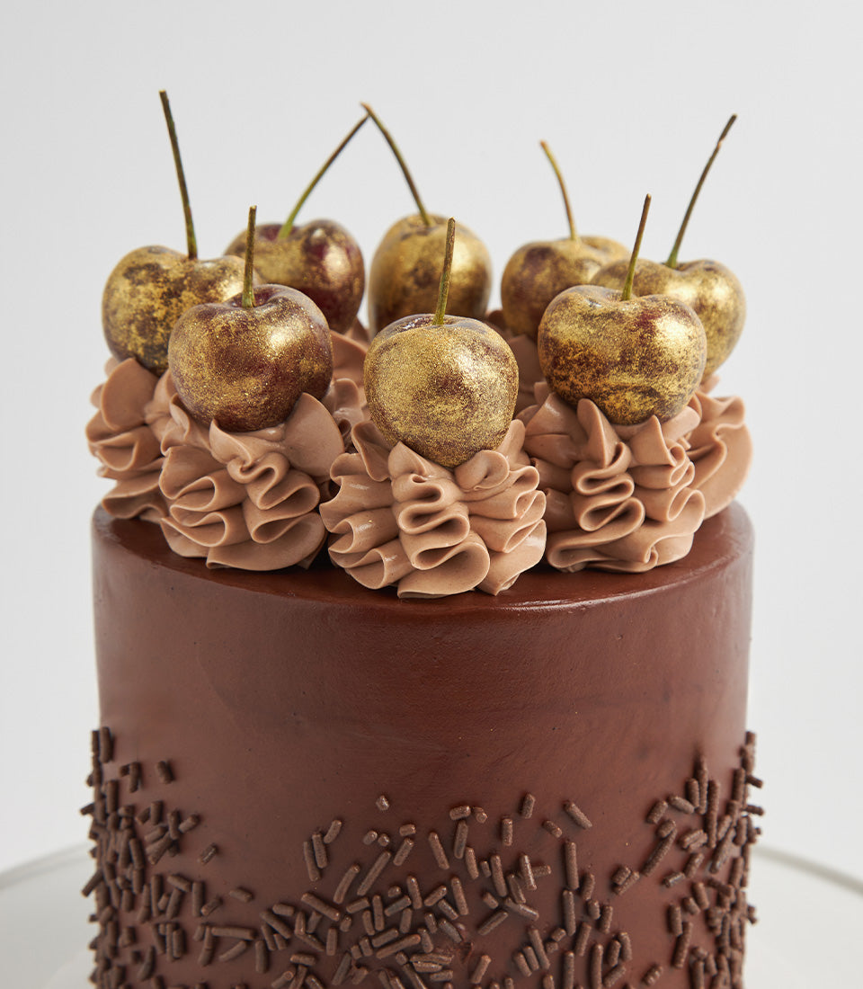 Rich chocolate layer cake with ruffled frosting, chocolate sprinkles, and gold-dusted cherries for birthdays