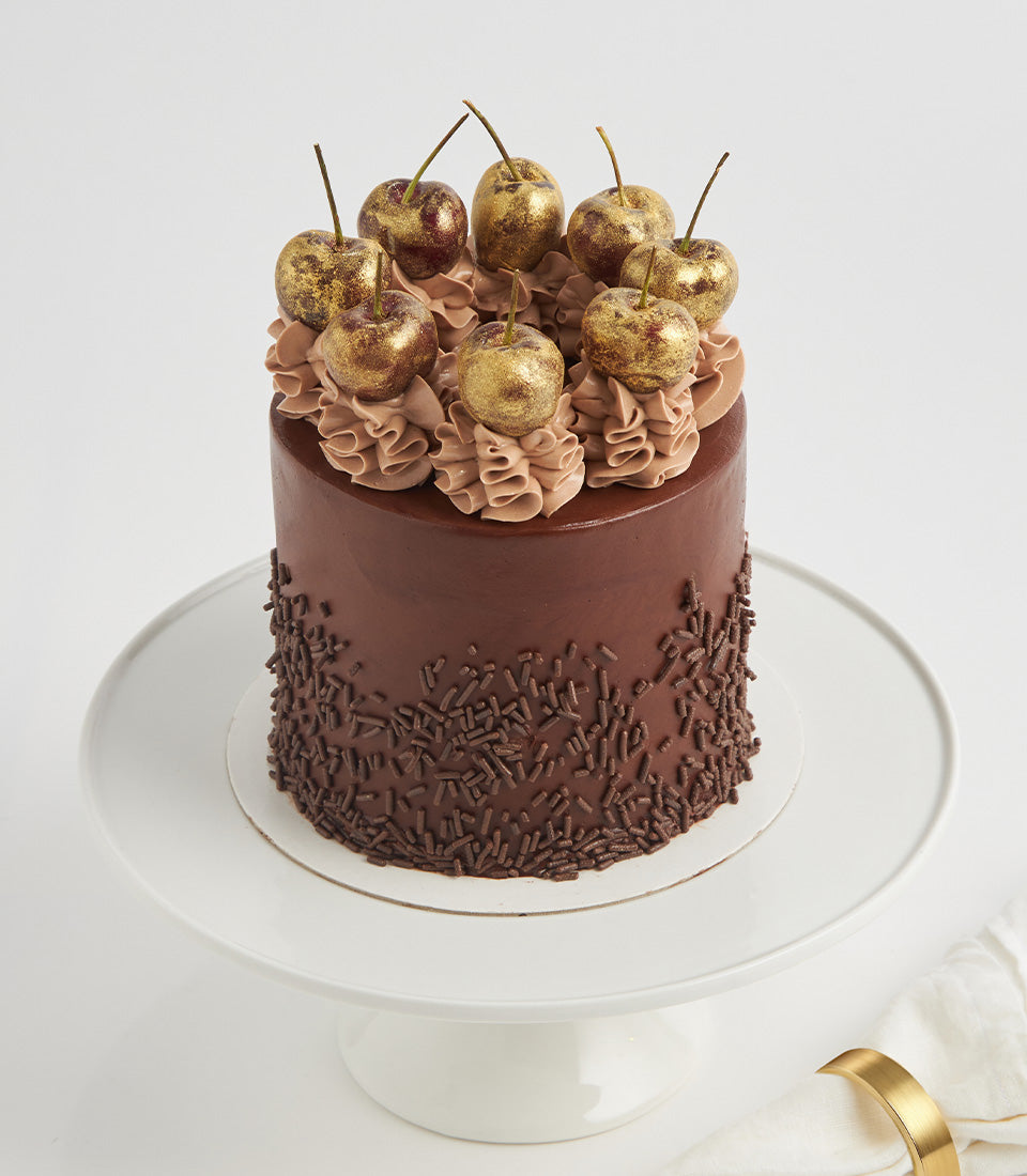 Rich chocolate Nutella layer cake with golden-dusted cherries and cocoa sprinkles on ceramic stand