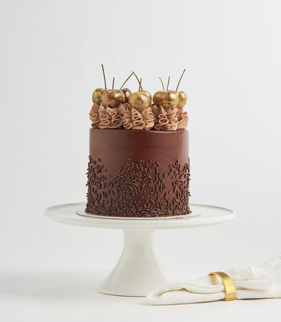 Decadent chocolate Nutella layer cake with dark ganache, golden glitter cherries, and chocolate sprinkles on ceramic stand