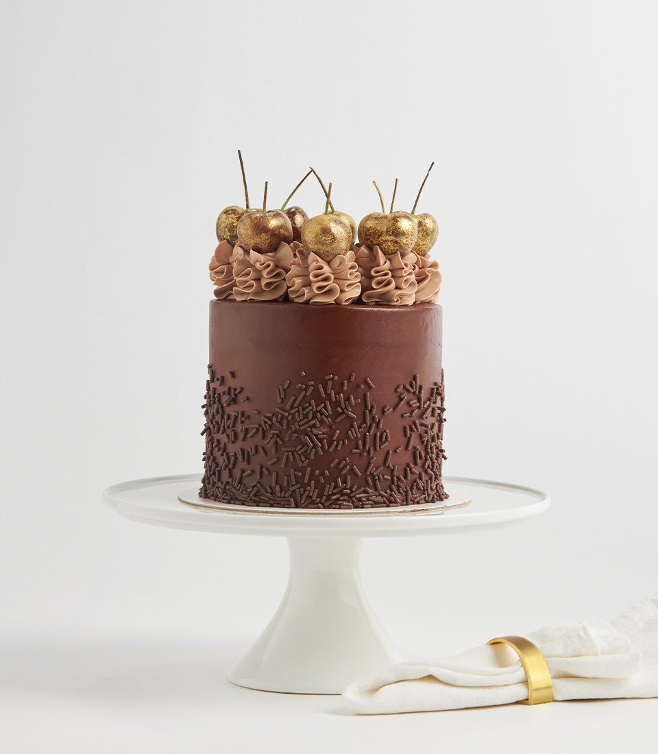 Decadent chocolate Nutella layer cake with dark ganache, golden glitter cherries, and chocolate sprinkles on ceramic stand
