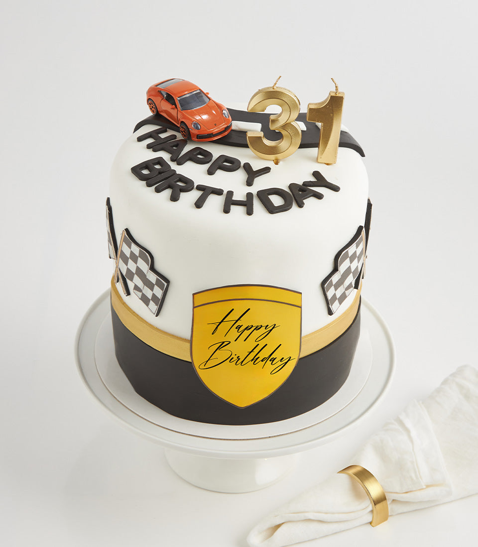 Speed Racer black and white two-tier birthday cake with toy sports car, checkered flags, and gold accents
