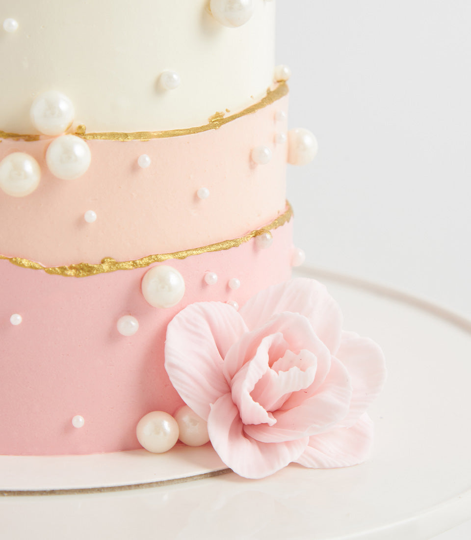 Three-tiered pearl birthday cake with cream-to-pink ombre tiers, white edible pearls, and sugar flower detail