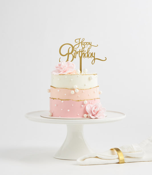 Three-tier gradient pink and white birthday cake with pearl beads and gold accents on ceramic stand