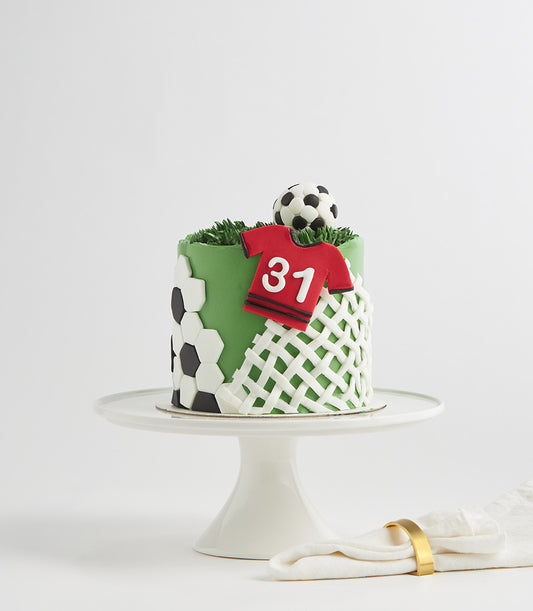 Green football field birthday cake with soccer ball fondant detail and number jersey on white stand