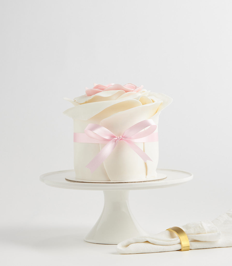 White fondant layer cake with blooming rose design, pink petal center, and pink satin ribbon bow