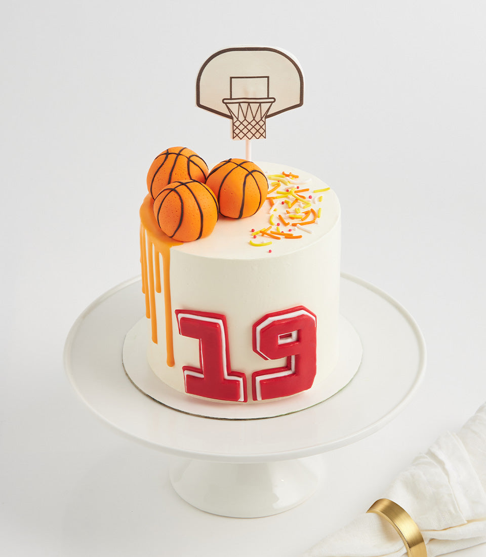 White basketball-themed birthday cake with orange drip, hoop topper, and number "19" decoration