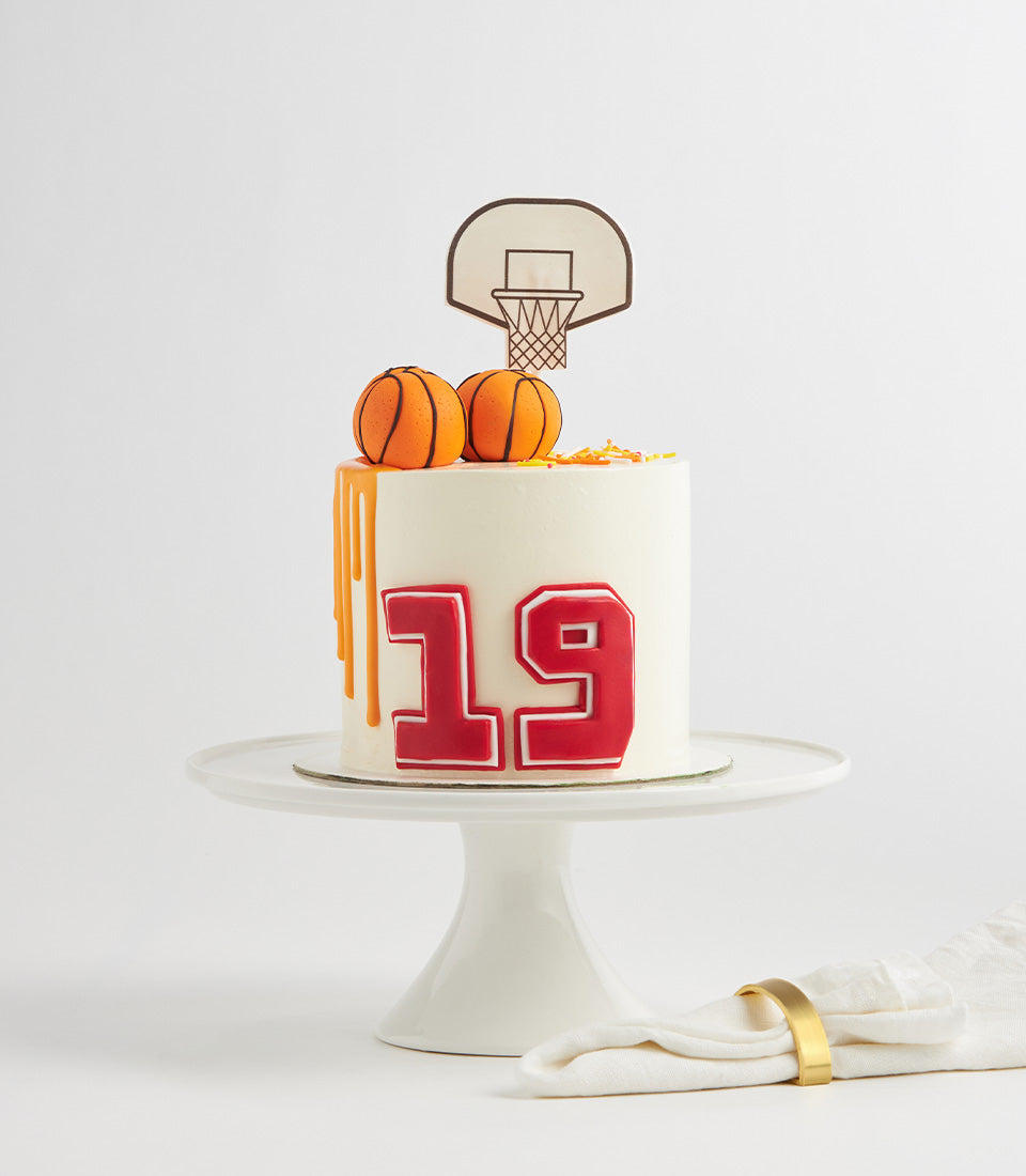 White birthday cake with orange basketball drip, number 19, and miniature basketballs on white stand