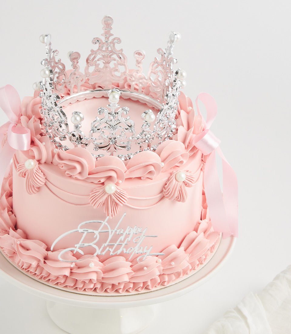 Pastel pink princess crown birthday cake with pearl-embellished tiara, rosette piping, and silver Happy Birthday topper