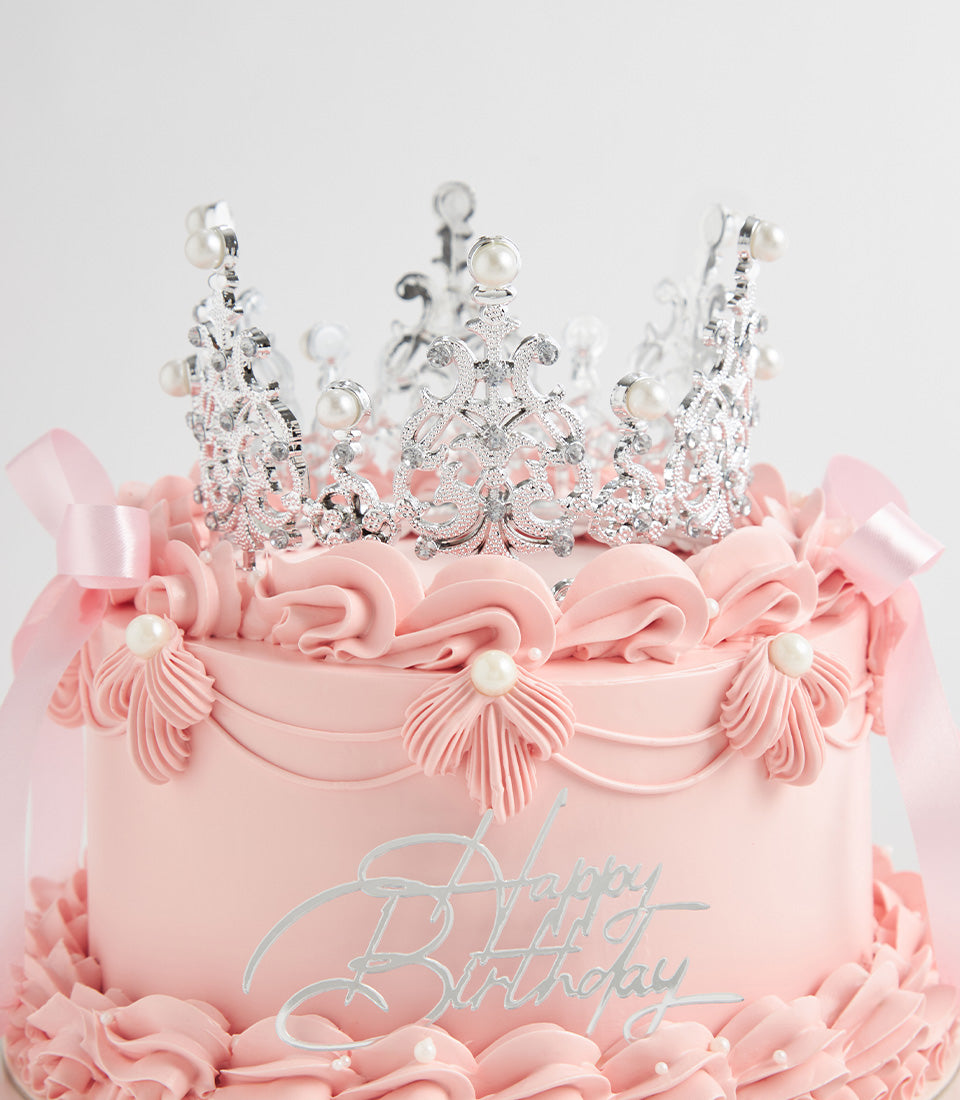 Two-tiered pink birthday cake with silver crown, pearl details, and satin ribbon bows