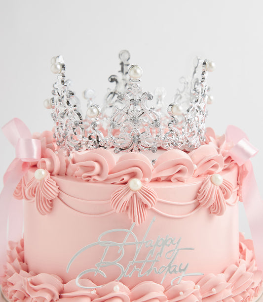 Two-tiered pink birthday cake with silver crown, pearl details, and satin ribbon bows