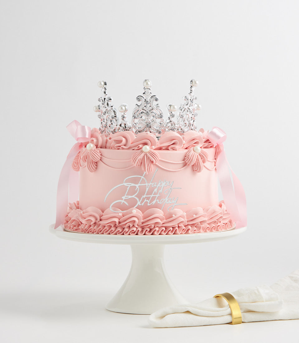 Pink layered birthday cake with silver crown topper and pearl details on white stand