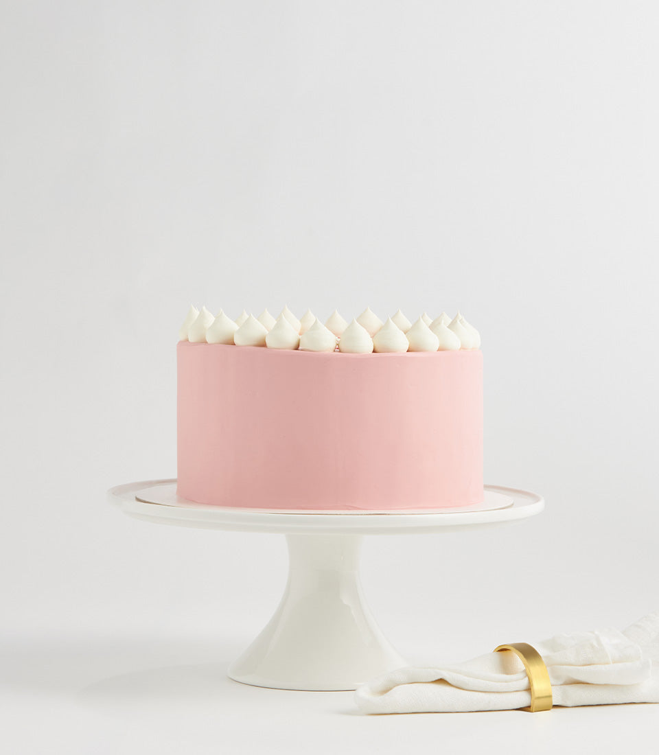 Light pink layer cake with white frosting and strawberry filling on ceramic stand