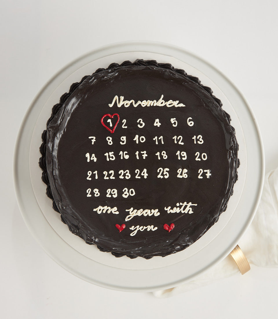 Dark chocolate anniversary calendar cake with November dates and "one year with you" message on ceramic stand