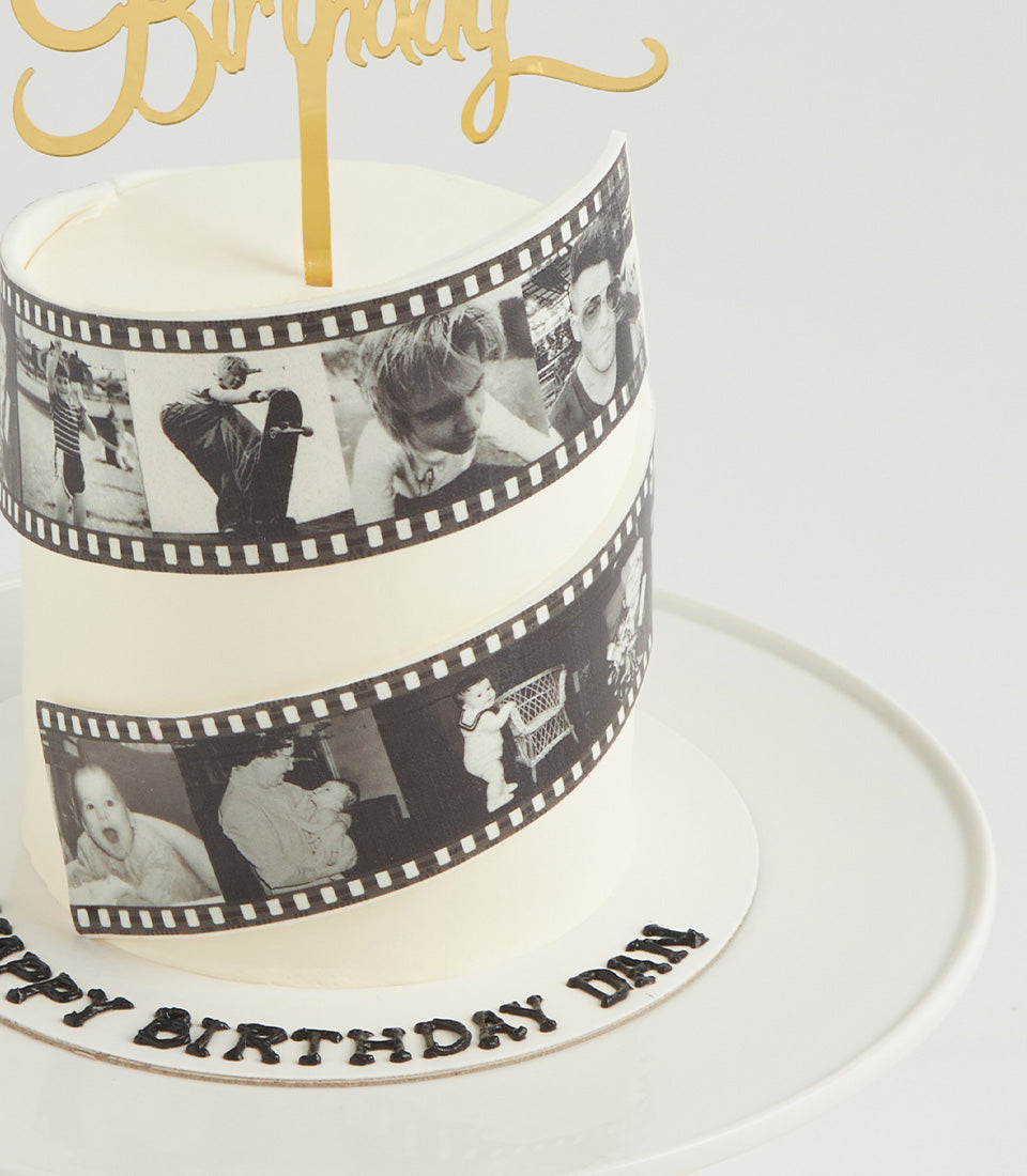 White round birthday cake with black film strip photo design wrapping the sides, personalized name inscription, and gold