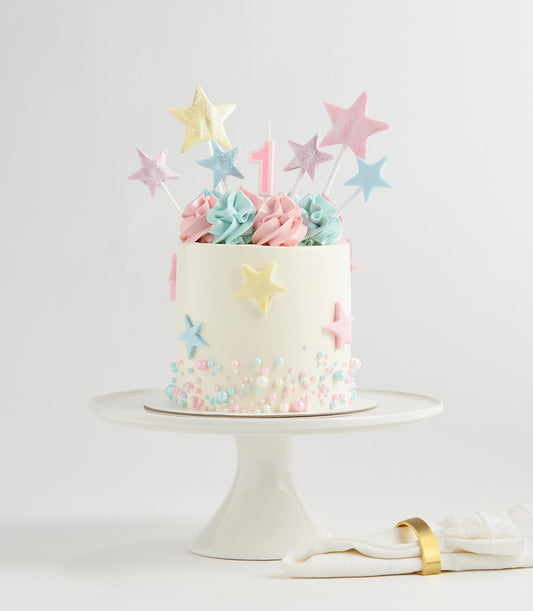 Pastel star two-tier birthday cake with fondant stars and sprinkles on white cake stand