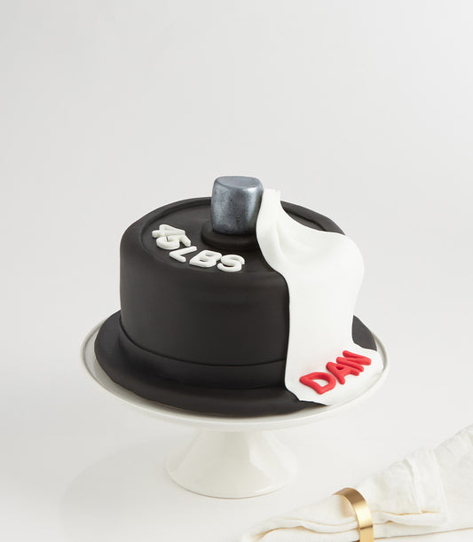 Black fondant barbell weight plate cake with silver center, white "45 LBS" lettering, and personalized towel detail for
