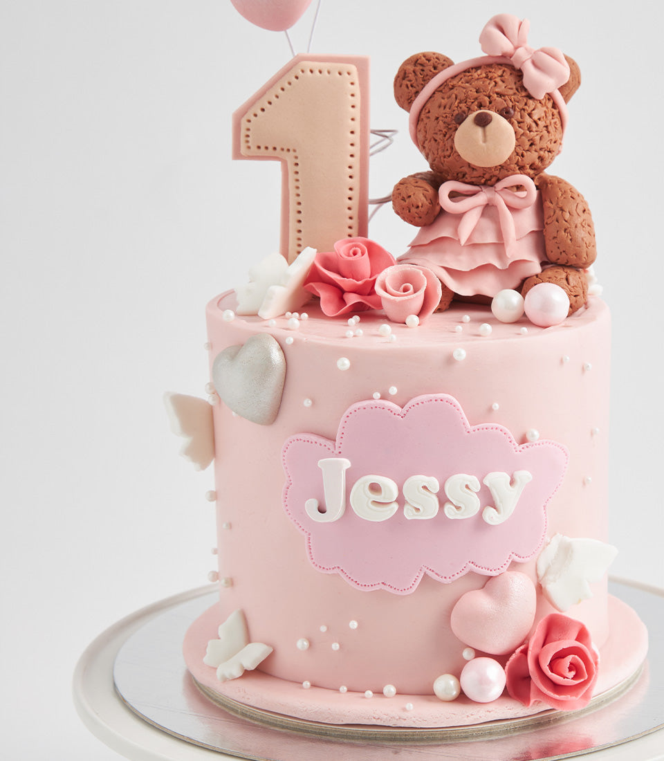 Pink first birthday cake with teddy bear, roses, and personalised cloud plaque