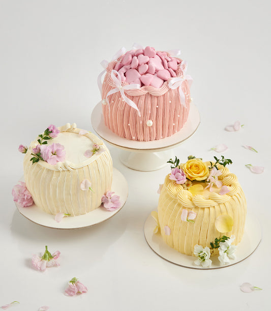 Sunshine yellow mini celebration cake topped with fresh rose and pink flowers, textured ruffle sides, artisan British-style