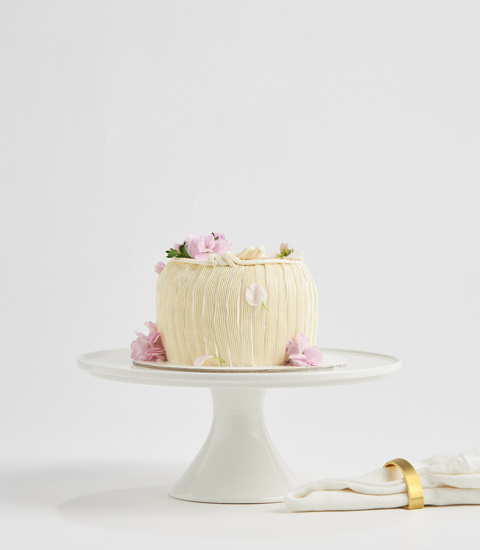 Lemon cream layer cake with pink flowers and textured frosting on white cake stand