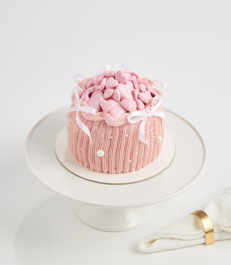 Pink heart-shaped candy birthday cake with white satin bows and pearl beads on ceramic stand