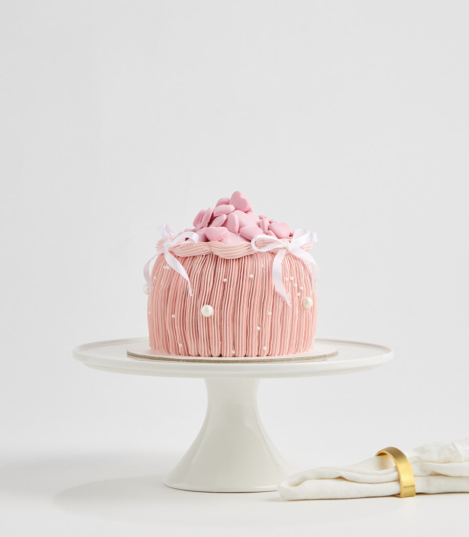 Pink heart bow layer cake with pearl details and strawberry frosting for birthday celebrations