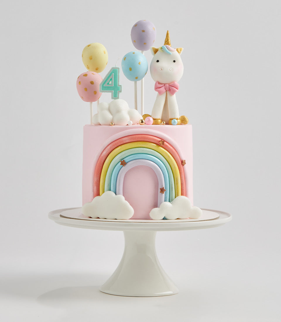 Pastel rainbow unicorn birthday cake with fondant arch, golden stars, and number 4 candle for kids