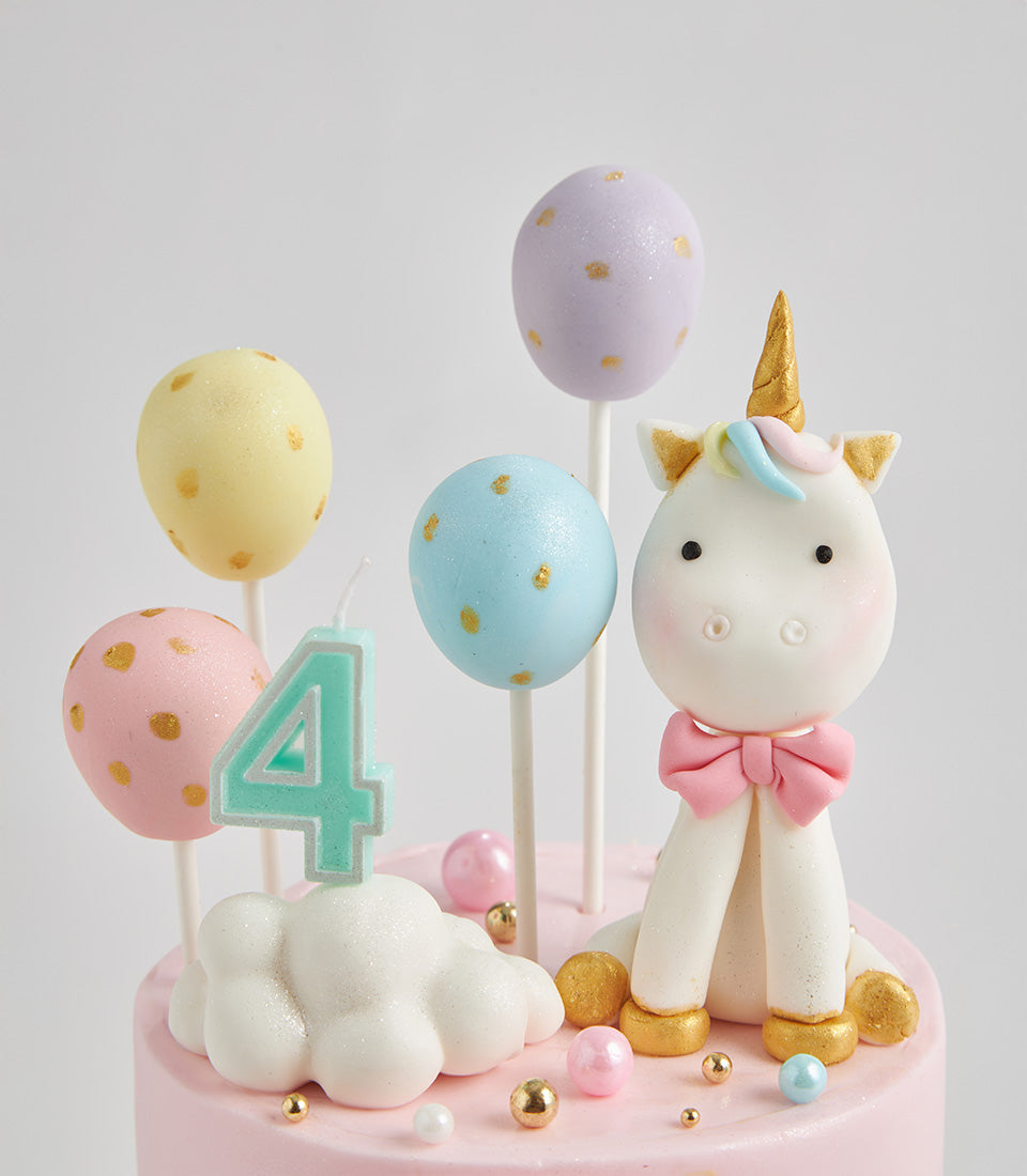 Pastel rainbow unicorn birthday cake with fondant details, golden horn, cake pops, and number 4 candle for kids' celebrations