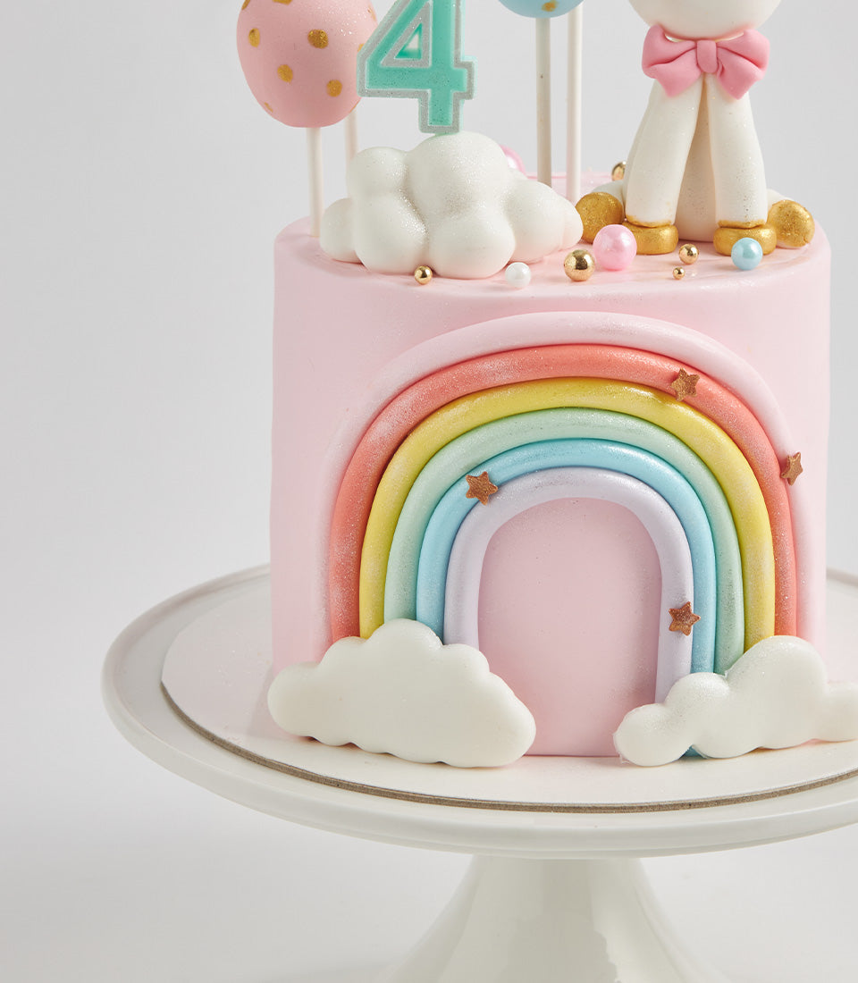 Light pink fondant birthday cake with pastel rainbow, white clouds, unicorn topper and number 4 for children