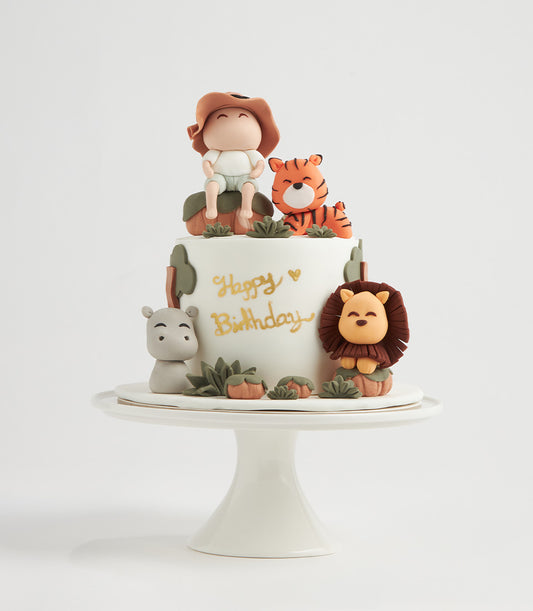 White two-tier jungle-themed birthday cake with fondant safari animals, tiger, lion, and hippo on ceramic stand