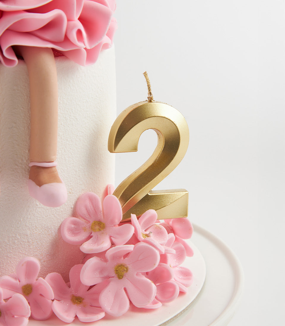 White tiered birthday cake with ballet-themed doll, pink sugar flowers, and number 2 candle for second birthday