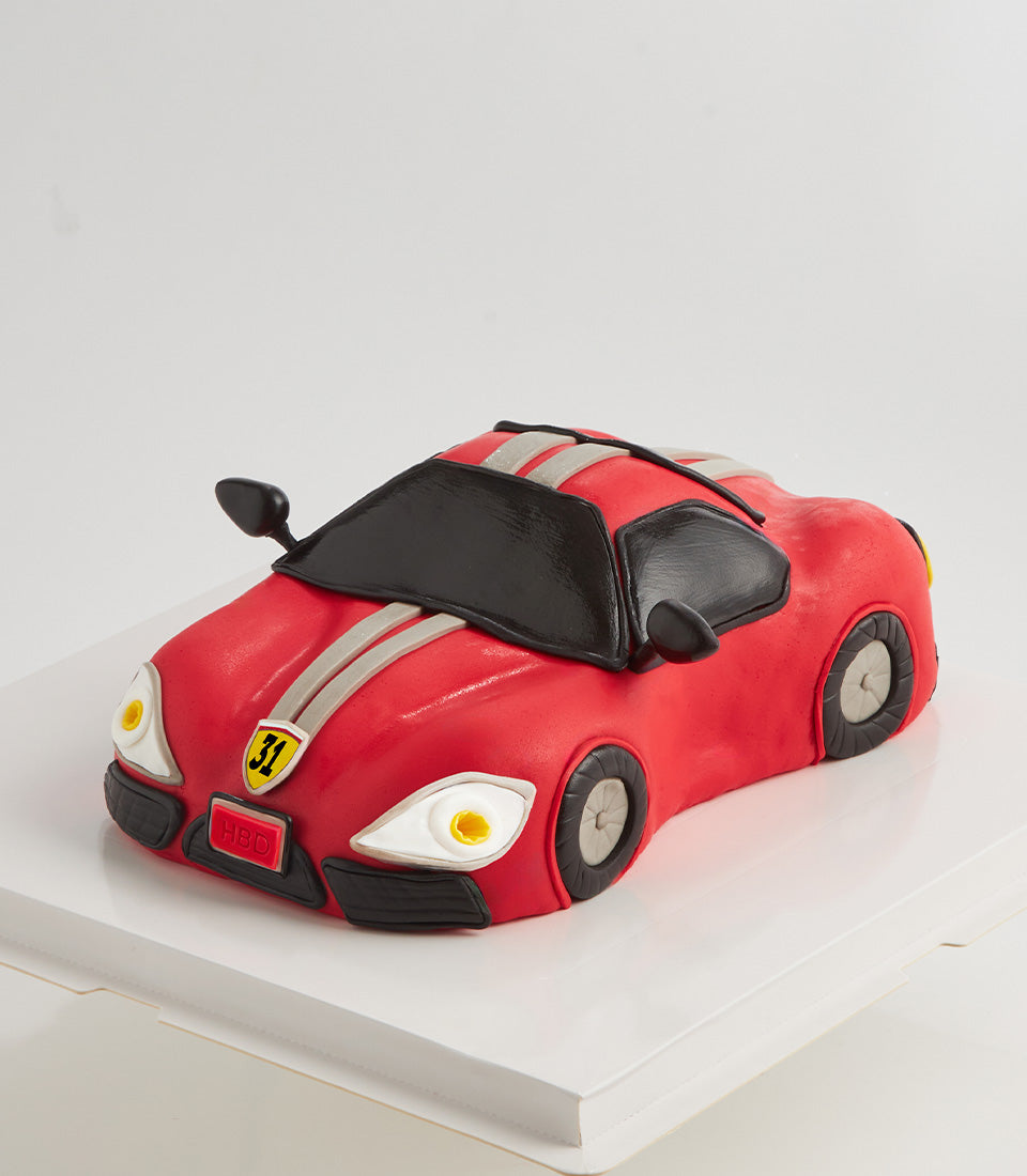Red sports car-shaped birthday cake with black accents, grey stripes, and HBD license plate detail