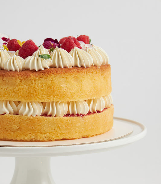 Raspberry buttercream sponge cake with fresh raspberries and edible flowers on white cake stand
