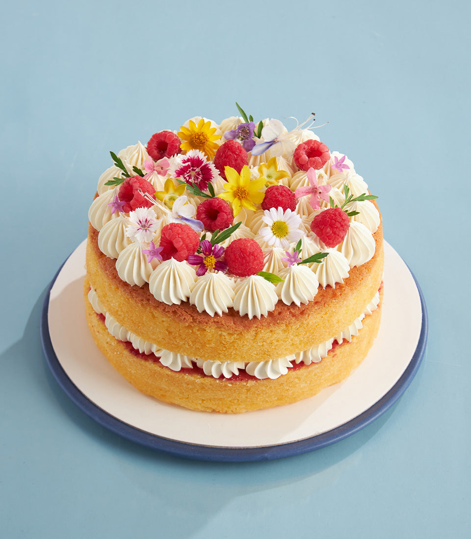 Two-tier raspberry buttercream sponge cake with fresh berries and edible flowers, less sweet artisan baking
