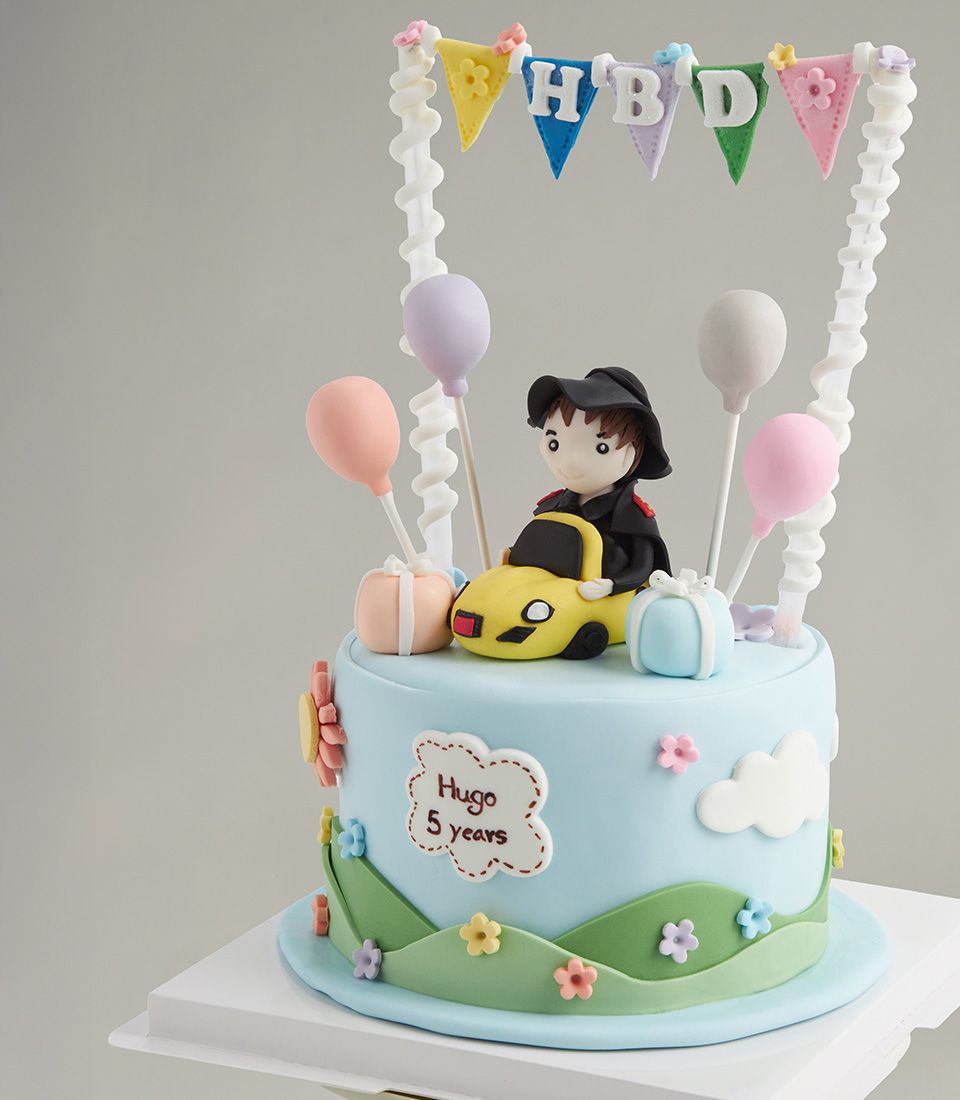 Light blue fondant birthday cake with yellow sports car, boy figure, and pastel balloons for kids' celebration