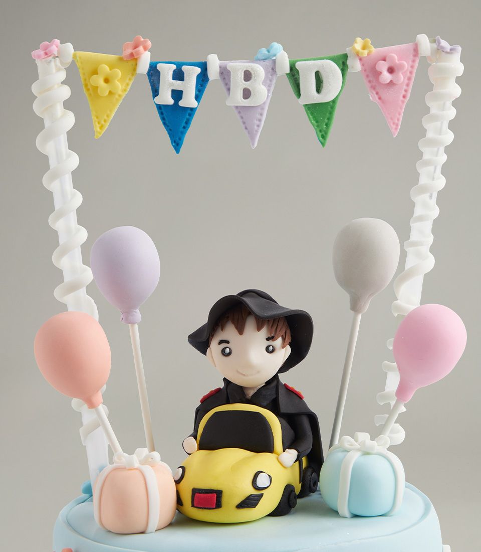 Fondant birthday cake topper with colorful HBD banner, yellow car with figure, pastel balloons and gifts on light blue base