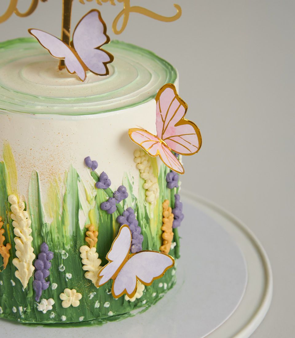 Butterfly Garden Birthday Cake with white frosting, floral design, and gold butterfly toppers on cake stand
