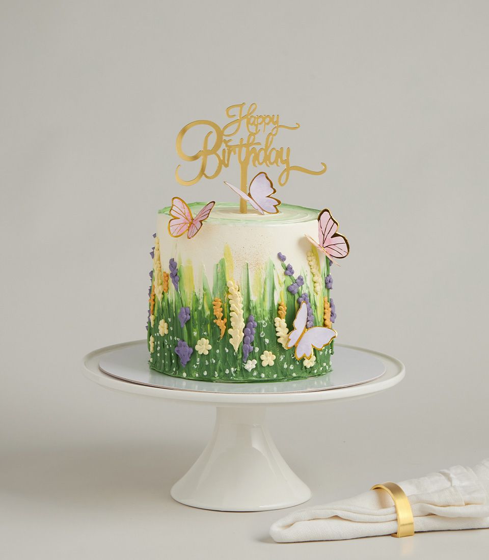 Vibrant green buttercream birthday cake with purple, yellow wildflowers and pink butterfly decorations on ceramic stand