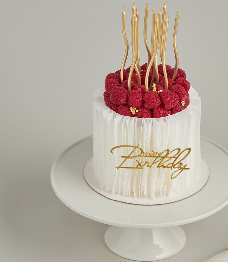 Raspberry Crown Wafer Paper Cake with gold candles and fresh berries on white cake stand
