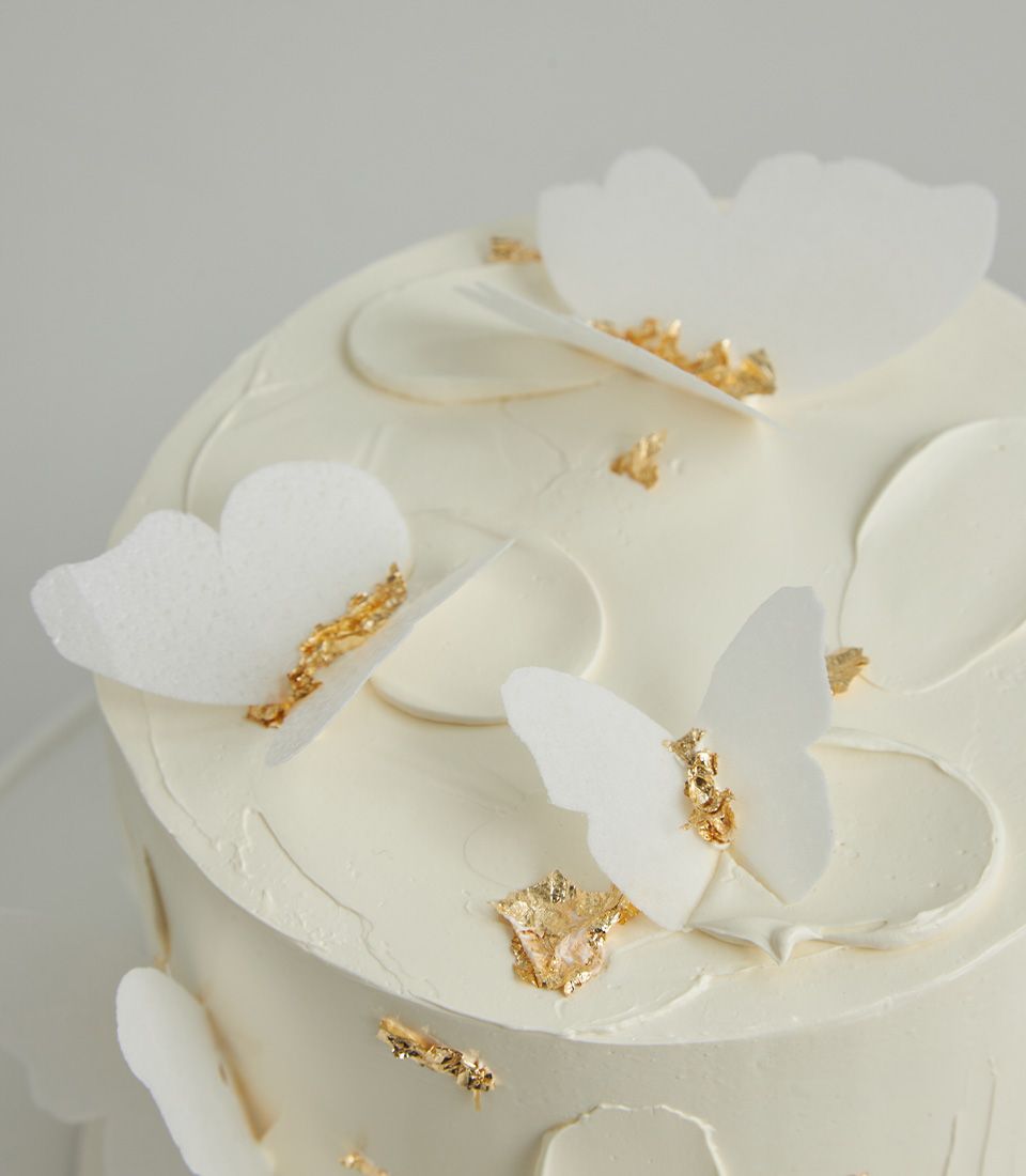 Elegant white buttercream cake with delicate butterfly decorations and gold leaf accents for celebrations