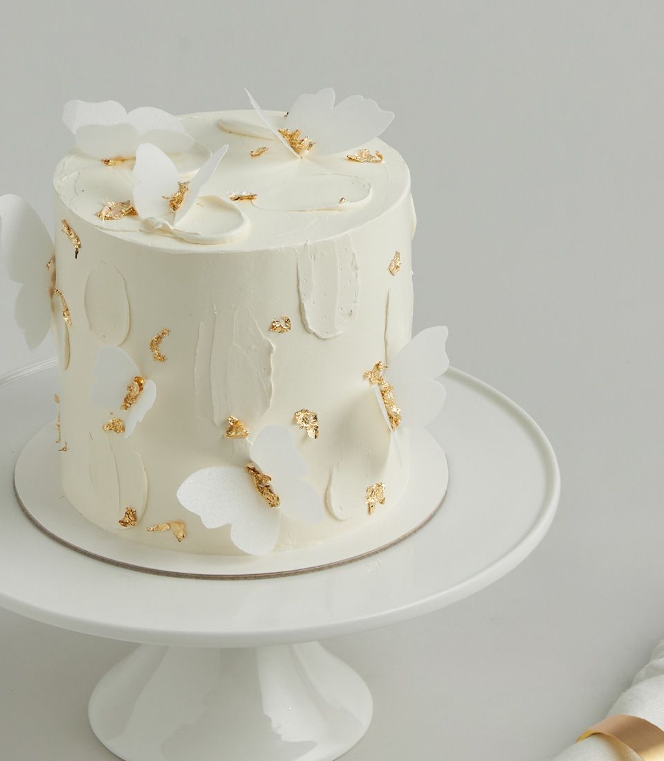 White frosted birthday cake with delicate butterfly and gold leaf decorations, elegant celebration dessert
