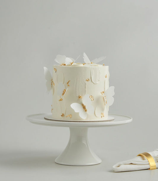 White layer cake with delicate butterfly cutouts and gold leaf, elegant celebration dessert