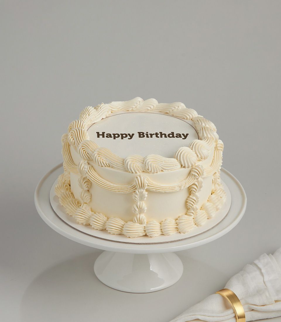Classic cream birthday cake with piped frosting swirls and happy birthday message on ceramic stand