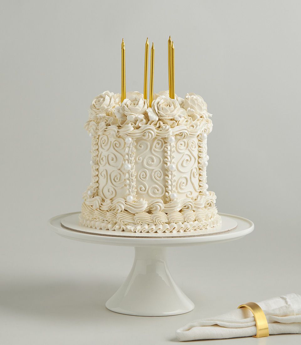 White buttercream vintage celebration cake with piped rosettes and pearl details, gold candles