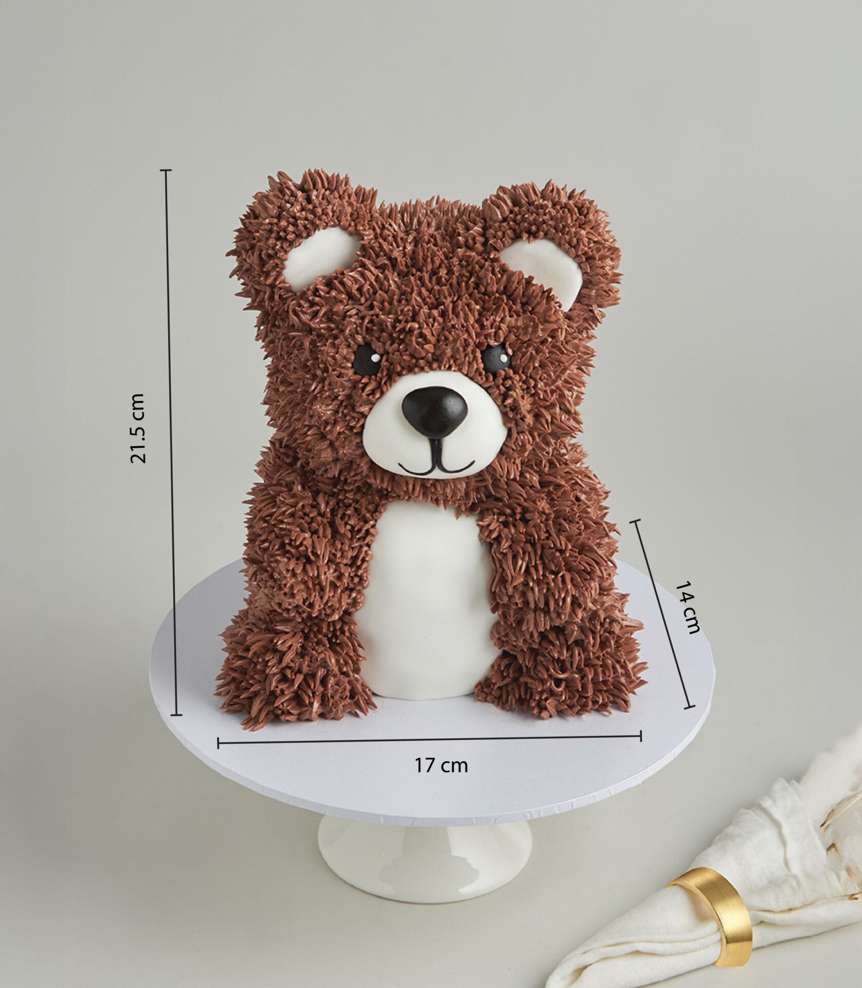Brown teddy bear cake with white details, textured frosting, black features, on white pedestal stand