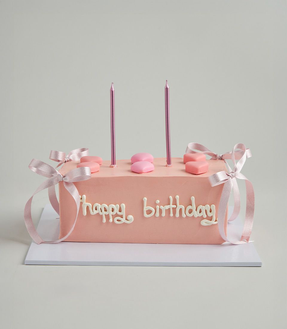 Pink ribbon heart birthday cake with strawberry frosting and metallic candles, artisan celebration cake from Charlotte Bakery