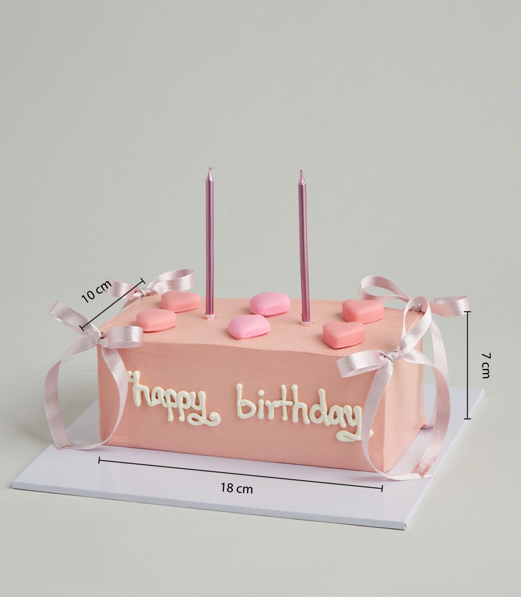 Light pink layer cake with white icing, heart candies, and pink ribbon bows for birthday celebration