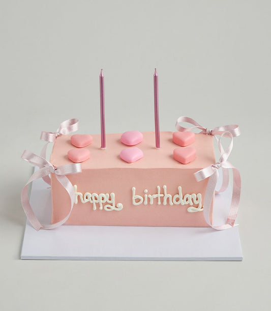 Light pink layer cake with heart candies, ribbon bows, and metallic candles for birthday celebrations