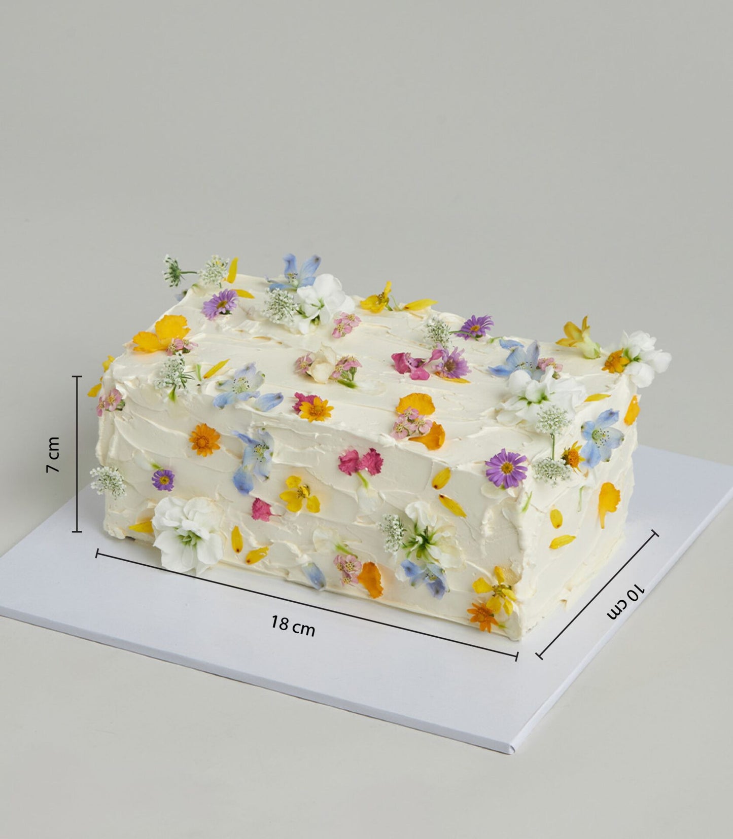 White buttercream layer cake adorned with edible flowers in yellow, pink, purple, and blue petals